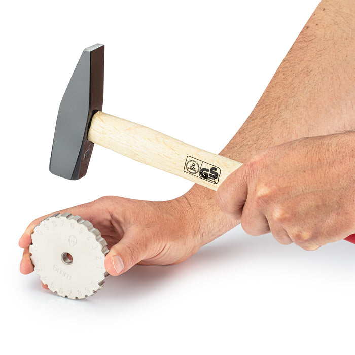 Image of a person holding a steel striking wheel in their right hand while their left hand holds a hammer, demonstrating the manual marking process using a striking wheel.